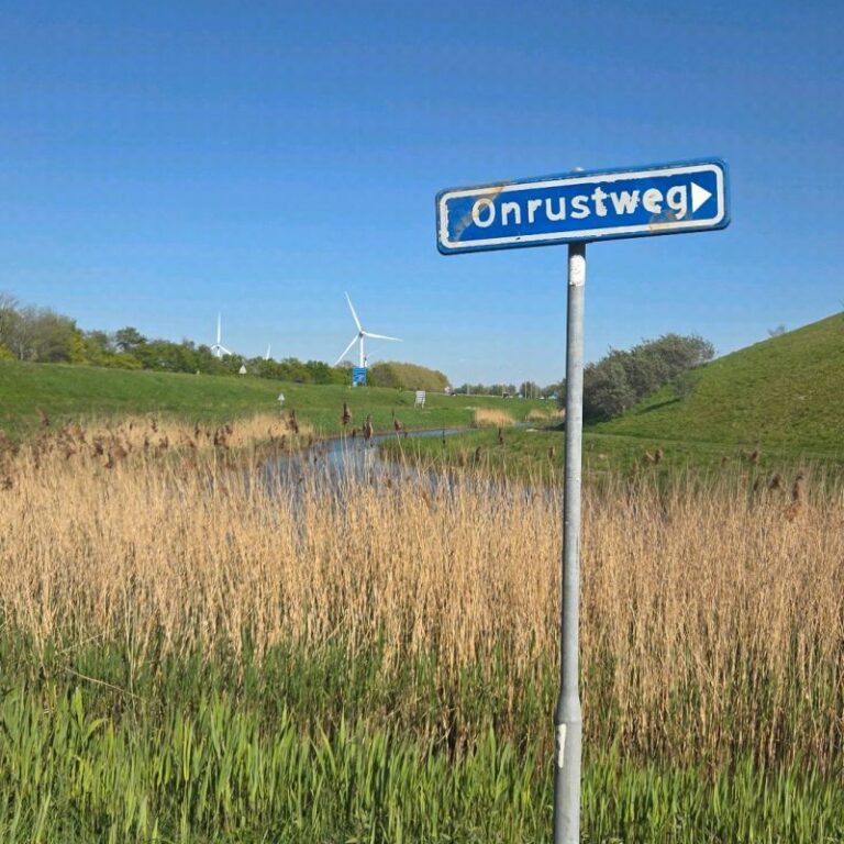 Straatnaambord Onrustweg langs een groene dijk met windmolens